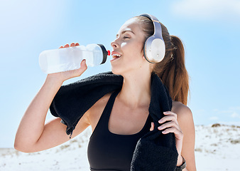 Image showing Beach, workout and drinking water with headphones music for exercise, fitness and training break. Wellness, relax and sport woman streaming audio and resting body after cardio with water hydration.