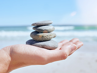 Image showing Hand, stones pile and beach with a woman holding little rocks by the ocean for balance, wellness or zen. Nature, earth and mindfulness with a rock stock in the palm of a female on the sand by the sea