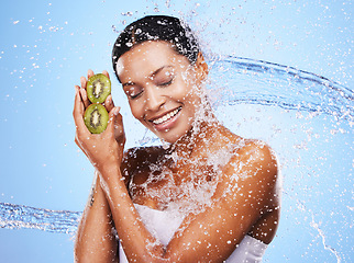 Image showing Water splash, kiwi and skincare of woman in studio isolated on a blue background. Healthcare, wellness and hygiene of female model from India with fresh and clean fruit for antioxidants or vitamin c.