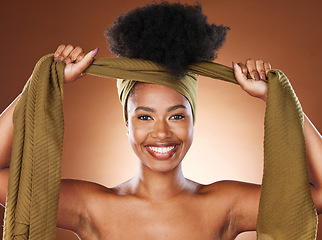 Image showing Face, beauty and black woman with hair scarf in studio on brown background. Fashion, haircare and happy female model tying her afro with fabric head wrap for unique hairstyle and healthy conditioner.