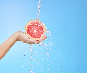 Image showing Hand, grapefruit and water splash for skincare nutrition, wellness or cosmetics against a blue studio background. Person hold citrus fruit in healthy, hydration or hygiene for natural vitamin C skin