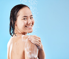 Image showing Shower, woman and hygiene for wellness, smile and happy with cleaning, water and soap against blue studio background. Portrait, young female and lady doing scrub, washing and health with happiness.
