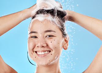 Image showing Woman, shampoo and shower in studio portrait with hair care, cleaning and smile by blue background. Model, hair and wellness with foam, soap or water for self care, cosmetics or beauty with happiness