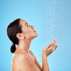 Image showing Water, shower and woman washing in a studio for body care, hygiene and to stop germs or bacteria. Health, wellness and Asian model cleaning her skin with aqua while isolated by a blue background.