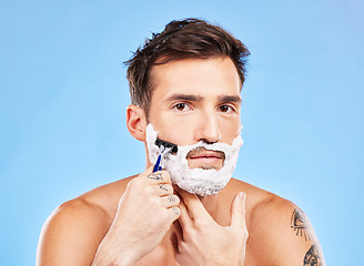 Image showing Portrait, shave and razor with a man model grooming in studio on a blue background for wellness or care. Face, skin and shaving with a handsome young male in the bathroom for facial hair removal