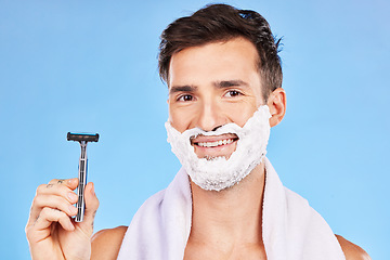 Image showing Man, razor and shaving with cream, happy and skincare while grooming beard, morning and cosmetic in blue studio background with mockup. Smile, clean and model cleaning facial hair for natural beauty