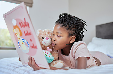 Image showing Reading, book and teddy bear with a black girl in bed, lying down to relax in the bedroom with her hobby. Children, books and education with a female kid telling her teddybear a story in their home