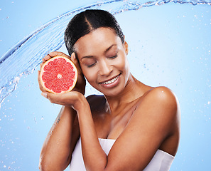 Image showing Grapefruit, black woman and water splash, beauty and skincare, vitamin c and healthy natural cosmetics of body wellness on studio blue background. Happy african model, wet citrus fruits and nutrition