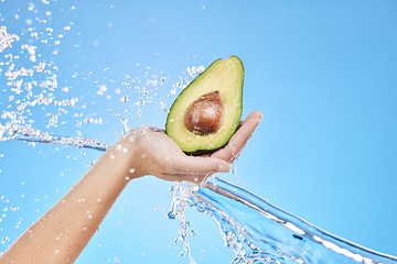 Image showing Hand, water and avocado for beauty splash and organic skincare product on a blue studio background. Avo, vegetable and natural produce for bodycare, skin care and nutrition or healthy diet