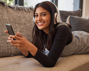 Image showing Woman, smile and phone listening to music with headset while relaxing on living room sofa. Portrait of happy female in relax and enjoying audio track, chatting or texting on smartphone on the couch