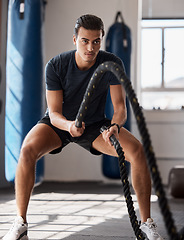 Image showing Fitness, man and rope exercise, training and workout, muscle, energy and wellness in sports gym. Young body builder guy swinging battle ropes with energy, speed and power, challenge and performance