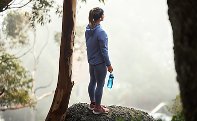 Image showing Hiking, mountain and forest woman with fitness goal, adventure and journey challenge achievement on rock or hill in winter. Sports, athlete and trekking person with water bottle walking in the woods