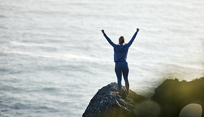 Image showing Success, ocean and rock with woman hiking for travel, freedom or training vacation. Heath, workout and silhouette with girl athlete on landscape adventure for winner, motivation or exercise in nature