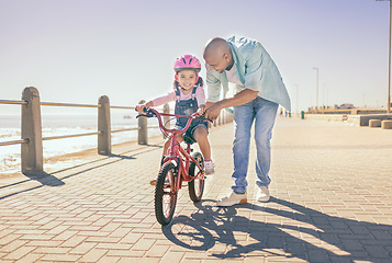 Image showing Father, child and bicycle with a girl learning to ride a bike on promenade by sea for fun, bonding and quality time on summer vacation. Man teaching his daughter or girl safety while cycling outdoor