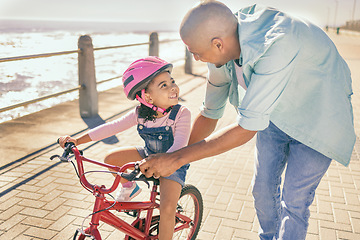 Image showing Father teaching his child to ride a bike at the beach while on a summer vacation, holiday or adventure. Happy, learning and man helping his girl kid with her bicycle while bonding in nature by ocean.