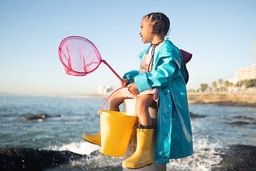 Image showing Girl, beach and fishing net with bucket, water and rock pool for outdoor adventure with boots, smile and ocean. Black child, sea and happy for fish, waves or sea in nature, learning and sunshine