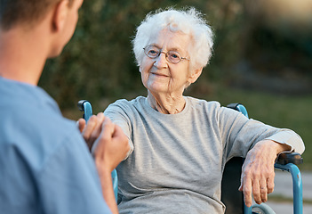 Image showing Senior woman, wheelchair and caregiver holding hands with patient for empathy, support and care outdoor for communication and air. Man nurse and old woman talking rehabilitation at nursing home