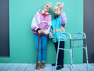 Image showing Phone, selfie and disability with senior friends posing for a photograph outdoor on a green wall background. Happy, mobile and walker with a mature woman and friend taking a picture together