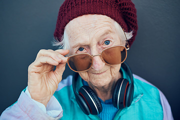 Image showing Senior woman, face and fashion sunglasses, vintage and 90s clothes, cool style and headphones with attitude against a wall outdoor. Elderly model, edgy attitude and retro portrait or retirement