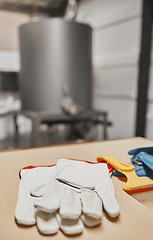 Image showing Gloves, beekeeping and production with equipment in an empty factory, plant or warehouse for honey extract. Farm, agriculture and sustainability with protective workwear on a table for manufacturing