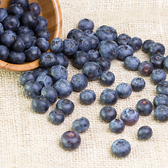 Image showing Blueberries in a wooden bowl scattered on a rustic table