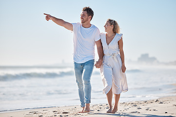 Image showing Couple, beach and travel holiday, love and happy smile, anniversary and date while walking, holding hands and point. Man, woman and summer vacation, happiness and together in nature and marriage life