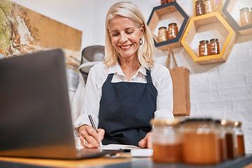 Image showing Laptop, small business and senior woman writing notes while doing inventory or online marketing. Happy, smile and elderly entrepreneur in a honey store working on admin or shop sales with a computer.