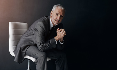 Image showing Portrait, manager or corporate with a business man sitting on a chair in studio against a dark background. Leadership, management and a senior male CEO in a professional suit for his executive career