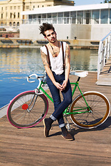 Image showing Bicycle, fashion and young man by the sea in a punk or rock outfit on an urban holiday. Tattoo, confidence and portrait of a serious grunge or edgy gen z male person with a bike by a lake boardwalk