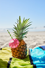 Image showing Cocktail, travel and closeup of a pineapple on a beach with alcohol on a towel for vacation. Summer, ocean and tropical organic fruit with a straw or paper umbrella on the sand for a seaside holiday.