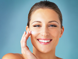 Image showing Skincare, portrait and happy woman with cream on face, cosmetics and product for makeup on blue background. Happiness, skin care and wellness for model with smile, beauty and lotion for facial glow.