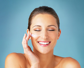 Image showing Skincare, smile and woman with cream on face, cosmetics and makeup product on blue background. Happiness, skin care and wellness for happy model with beauty, lotion and dermatology for facial glow.