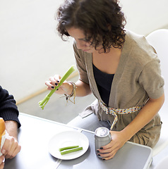 Image showing Health, diet and woman eating a celery stick for weightloss, wellness or vegetarian snack. Disappointment, upset and young female person with a green vegetable and beverage by a dining table at home.