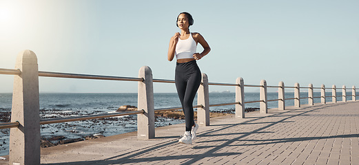 Image showing Fitness, woman run at beach and with headphones listening to music for health wellness. Training or exercise, marathon or lens flare and female person running along the promenade listen to radio
