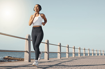 Image showing Fitness, woman run at beach and with headphones listening to radio with lens flare. Training or exercise, marathon or sportswear and female person running along the promenade listen to music