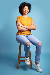 Image showing Portrait, arms crossed or happy woman sitting on stool in studio isolated on a blue background. Waiting on chair, confidence or proud African female person in South Africa with smile, style or afro