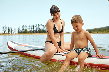 Image showing Lake, mother and son on paddle board, relax outdoor with summer holiday and travel with feet in water. Adventure, freedom and nature, woman and boy child in swimsuit, vacation and bonding together