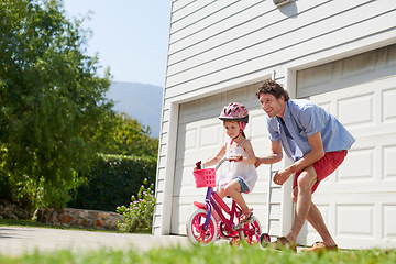 Image showing Father teaching child to ride a bike as support, trust and skill development outdoor of a home or house together. Parent, safety and happy dad care and help kid or girl learning to use a bicycle