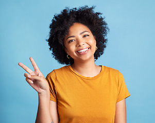 Image showing Peace sign, portrait of a woman with smile and against a blue background for satisfaction. Positivity or cheerful, health wellness and face of happy female person pose against studio backdrop