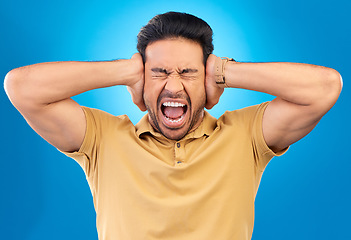 Image showing Man covering his ears while screaming in a studio for angry, upset or mad argument expression. Crazy, shout and young male person with an open mouth for loud voice gesture isolated by blue background