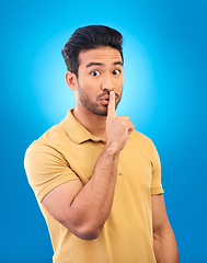 Image showing Man, studio portrait and secret with finger on lips for silence, quiet and stop noise by blue background. Young asian guy, student and icon to cover mouth for deal, confidential and privacy emoji