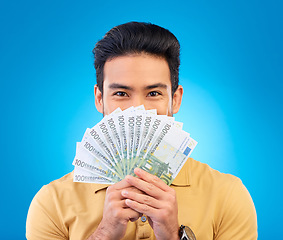 Image showing Money, winner and man cover face isolated on blue, studio background for winning, cash fan or financial loan. Lottery, bank and asian person winning bonus, budget secret or finance profit in portrait