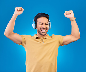 Image showing Headphones, success and man, winner or student excited for results, news or music, yes or energy. Happy, freedom and asian person listening to audio, podcast and celebration on studio blue background