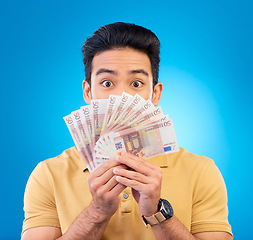 Image showing Money, fan and man with wow face isolated on blue, studio background for winning, cash surprise or financial profit. Lottery, gambling secret and asian person winning, bonus and cashback in portrait