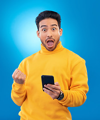 Image showing Winner, surprise and portrait of Asian man with phone in studio for online bonus, competition and prize. Success, smartphone and face of male person on blue background with promotion, winning and wow