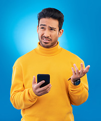 Image showing Scam, error and Asian man with a smartphone, confused and internet issue against a blue studio background. Male person, guy and model with a cellphone, doubt and decision with connection problems