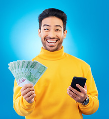 Image showing Man, phone and money fan in studio with prize, esports gambling or happy in portrait by blue background. Young asian guy, winner and cellphone with cash, fintech or crypto with profit, bonus or goals