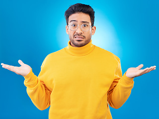 Image showing Confused, shrug and portrait of a man in a studio with an unsure, doubt or question expression. Uncertain, choose and headshot of a male model with a decision gesture isolated by a blue background.