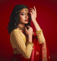 Image showing Portrait, celebration and Indian woman with fashion, traditional dress and jewellery against a red studio background. Face, female person or model with cultural clothes, religion and beauty with gold