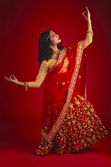 Image showing Fashion, dancer and Indian woman in a traditional dress, beauty and celebration on a red studio background. Female person, girl and model with a cultural outfit, dancing and confidence with religion